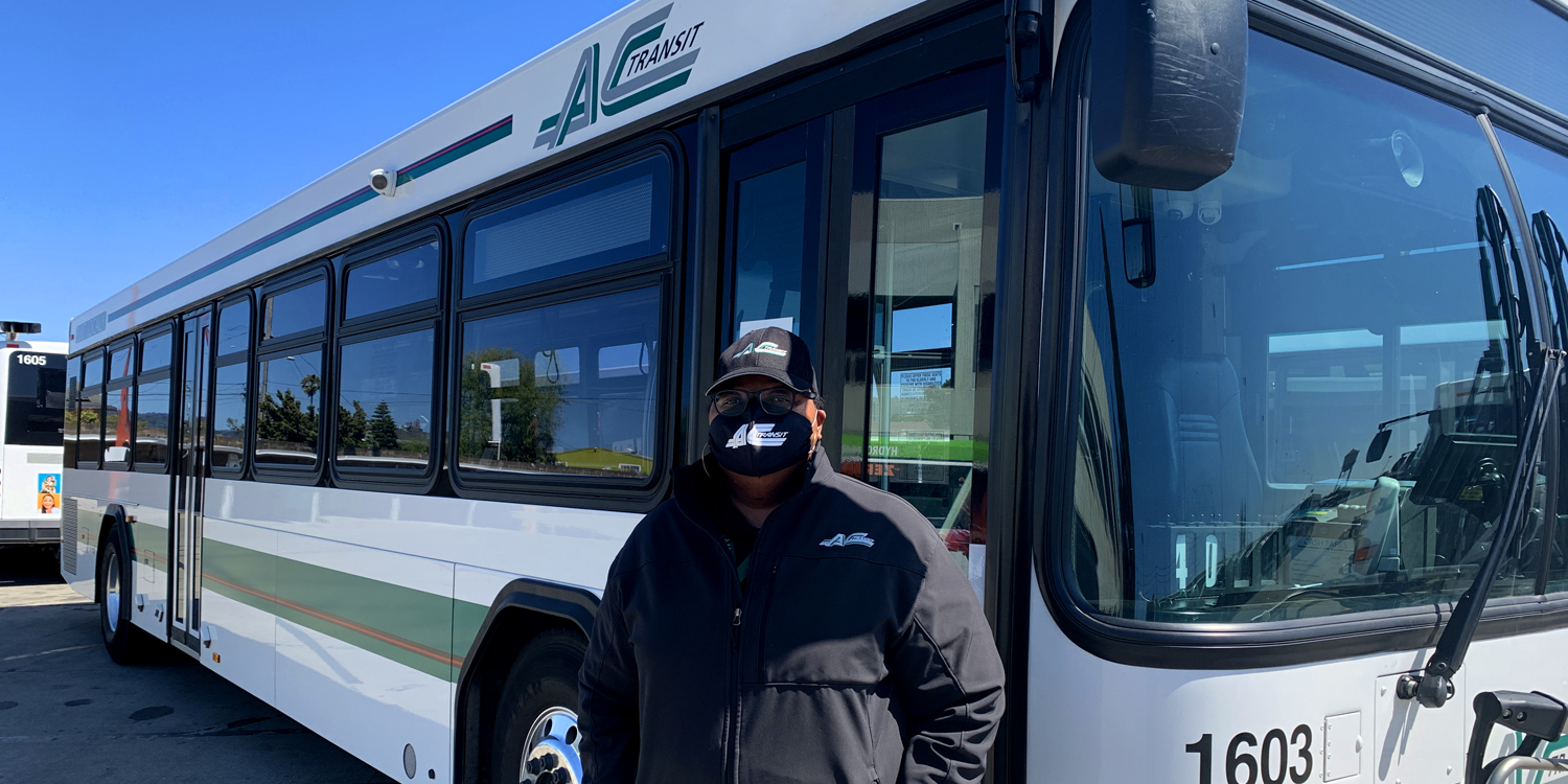 AC Transit bus operator is standing by the side of an AC Transit bus.