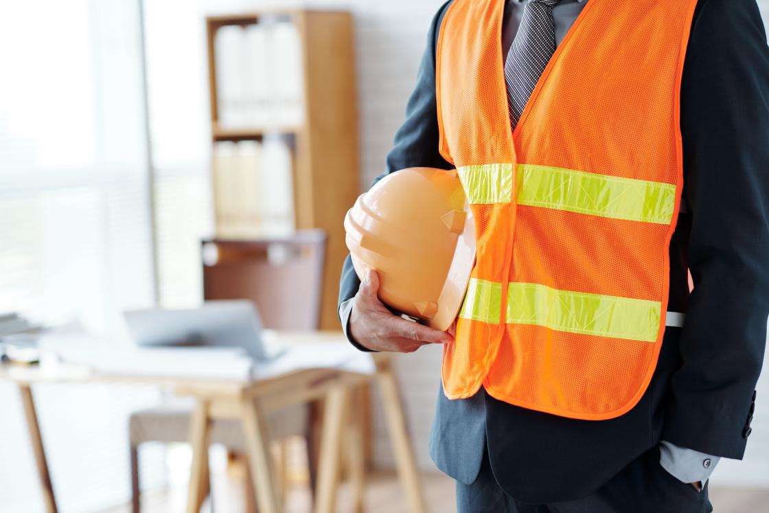 torso of man wearing safety vest and carrying a hard hat