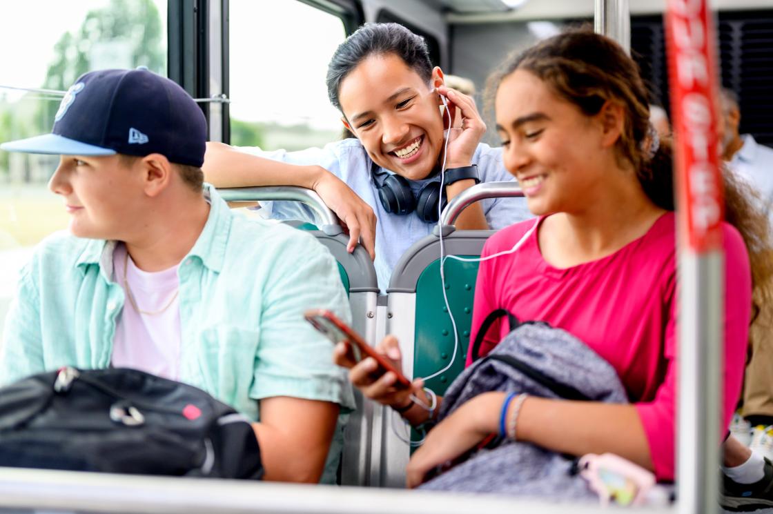 three students sit in seats and converse on the bus